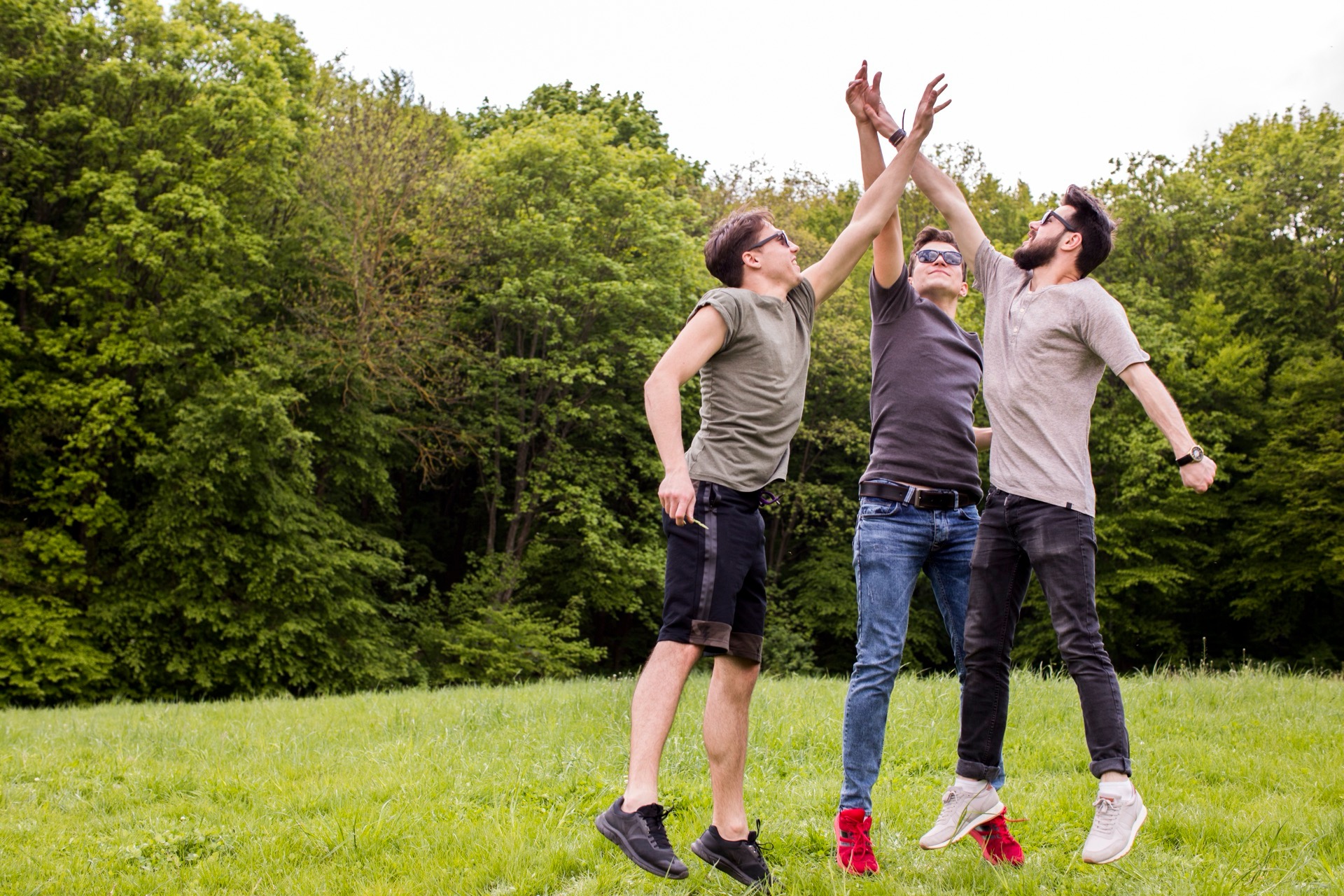 Tre män hoppar och ger varandra high five på en gräsäng vid skogen